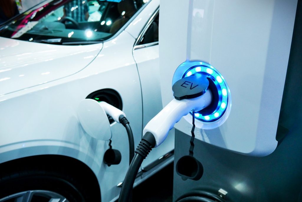 Electric vehicle recharges its battery by plugging into EV charging point.