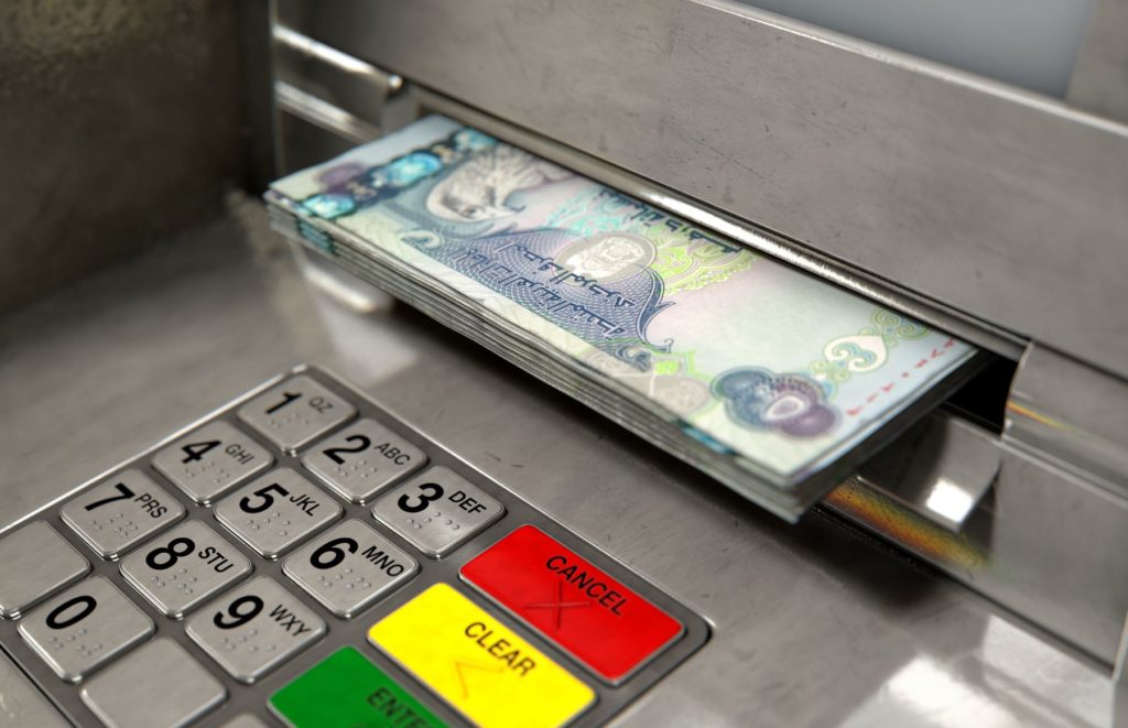 A closeup view of an ATM at a bank in the UAE with Dubai dirham banknotes being withdrawn from the cash slot to get car finance for private sale.