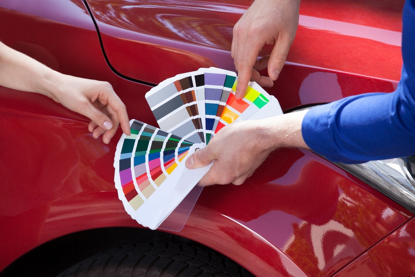 How to repaint a car: a mechanic showing colour samples to a customer against red car background