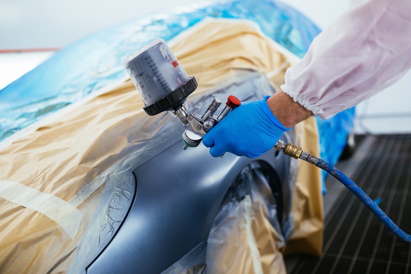 Mechanic with protective clothes painting a car using a spray compressor showing how to repaint a car.