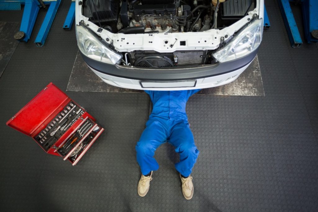 A difference between GCC specs and American specs can be the repair process; a mechanic lying and working under a white car to replace parts at the repair garage